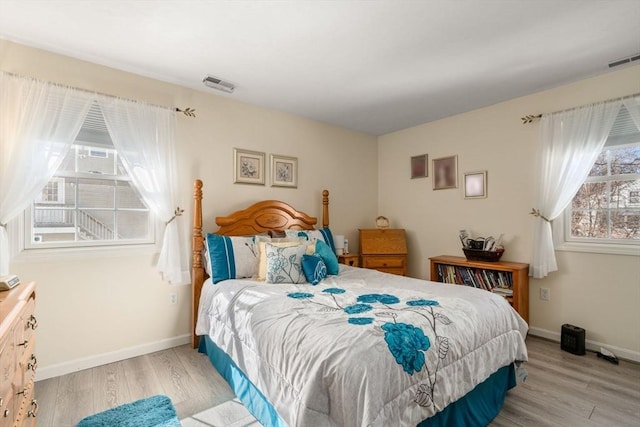 bedroom featuring baseboards, multiple windows, visible vents, and wood finished floors