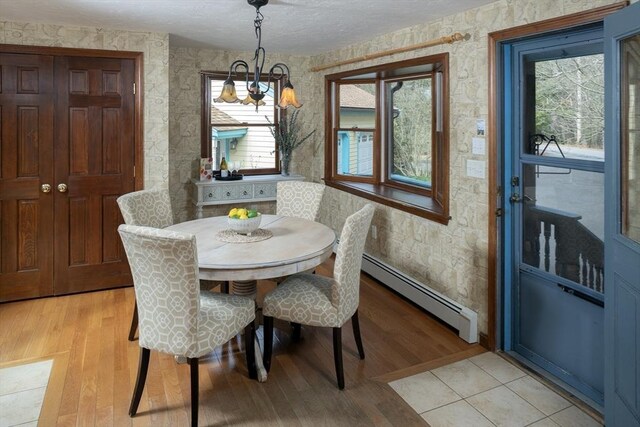 dining room featuring a chandelier, a textured ceiling, light wood-style flooring, wallpapered walls, and a baseboard heating unit