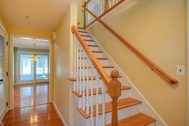 stairway with hardwood / wood-style floors and a notable chandelier