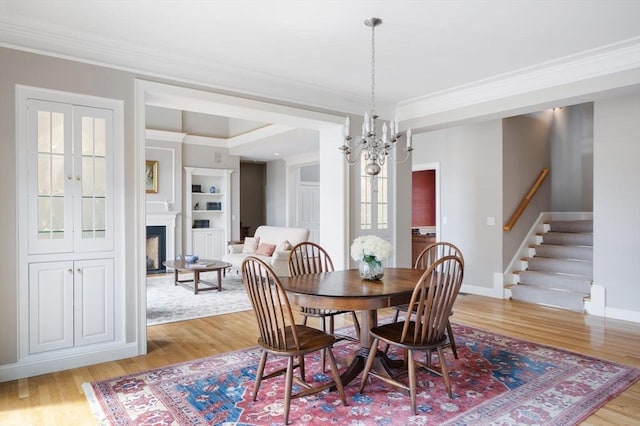 dining area featuring crown molding, stairs, light wood-type flooring, an inviting chandelier, and a fireplace