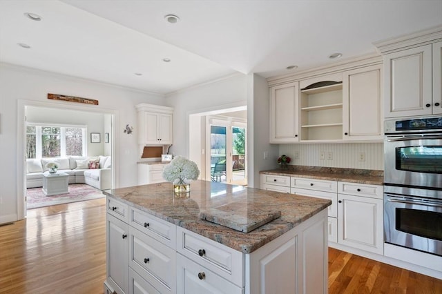 kitchen with light wood-style flooring, a center island, stone counters, open shelves, and double oven