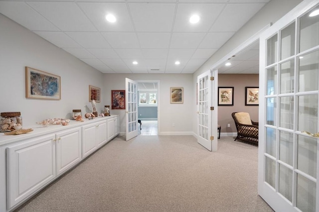 hall with a drop ceiling, baseboards, light carpet, and french doors