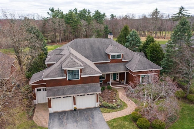 view of front facade featuring a chimney, a shingled roof, driveway, a porch, and a garage
