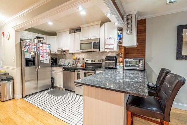 kitchen with appliances with stainless steel finishes, white cabinetry, decorative backsplash, ornamental molding, and kitchen peninsula