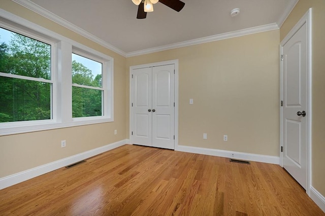 unfurnished bedroom with baseboards, light wood-type flooring, ornamental molding, ceiling fan, and a closet
