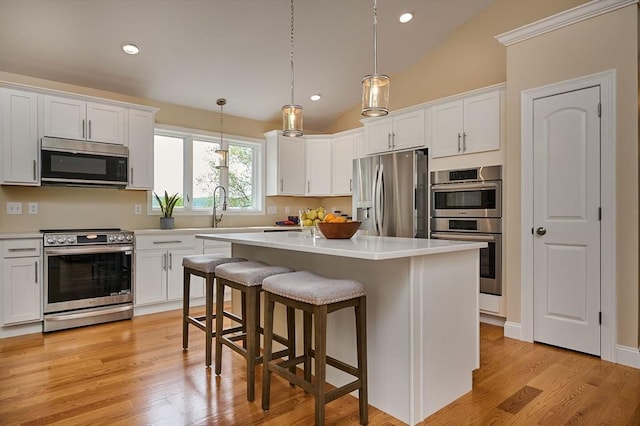 kitchen with appliances with stainless steel finishes, vaulted ceiling, white cabinets, a breakfast bar, and light countertops