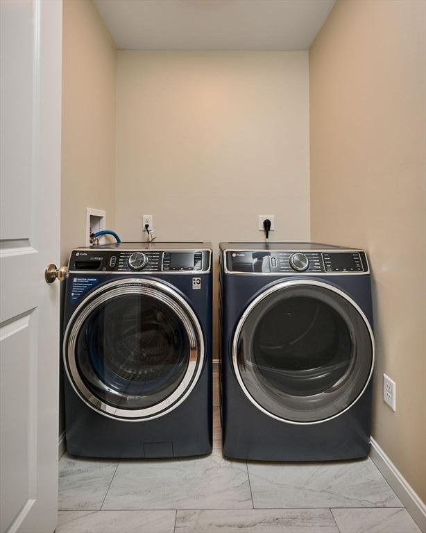 clothes washing area featuring washer and dryer, marble look tiles, and baseboards