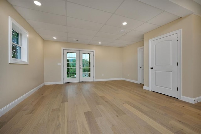 empty room featuring light wood-style floors, french doors, a drop ceiling, and baseboards