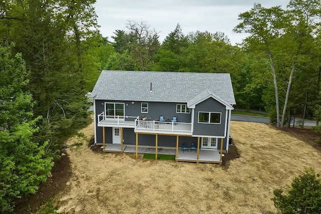 rear view of house with a deck, french doors, roof with shingles, and a forest view