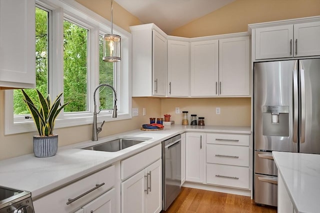 kitchen with stainless steel appliances, a sink, white cabinetry, and vaulted ceiling