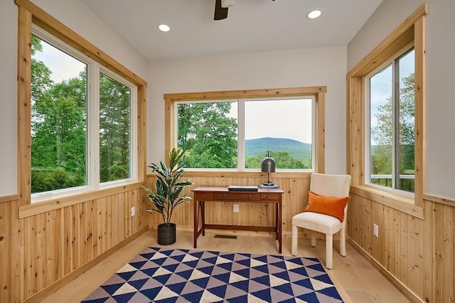 sitting room with wood walls, plenty of natural light, light wood finished floors, ceiling fan, and wainscoting