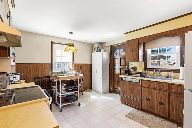 kitchen featuring wainscoting, dishwasher, a sink, light countertops, and wooden walls