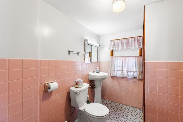 bathroom with a sink, wainscoting, toilet, and tile walls
