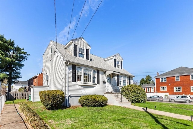 new england style home with a front lawn, roof with shingles, and fence