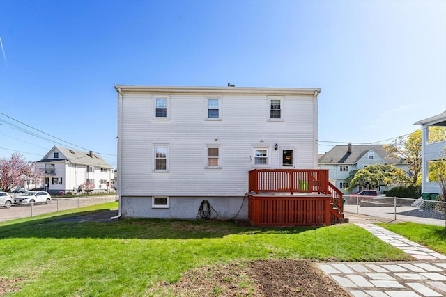 rear view of house with fence, a wooden deck, and a lawn