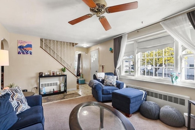 carpeted living area with a ceiling fan, stairs, arched walkways, and radiator