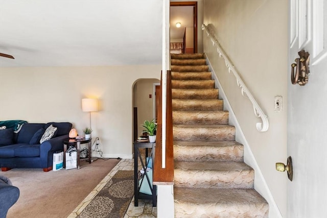 stairway with carpet floors, arched walkways, ceiling fan, and baseboards