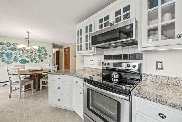 kitchen featuring white cabinets, wainscoting, glass insert cabinets, hanging light fixtures, and stainless steel appliances