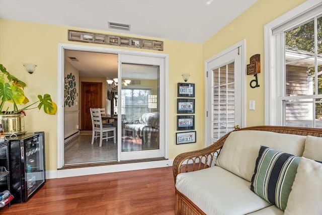 sitting room featuring beverage cooler, visible vents, wood finished floors, baseboard heating, and a chandelier