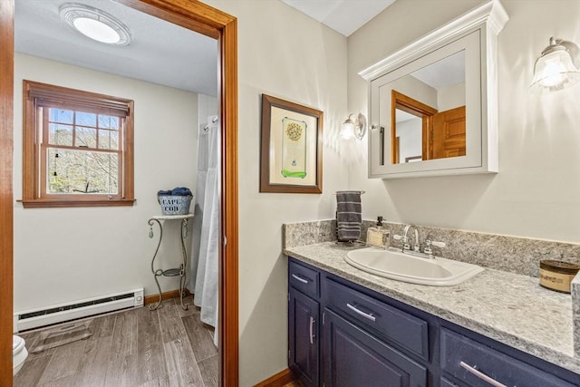 bathroom with baseboards, toilet, wood finished floors, baseboard heating, and vanity