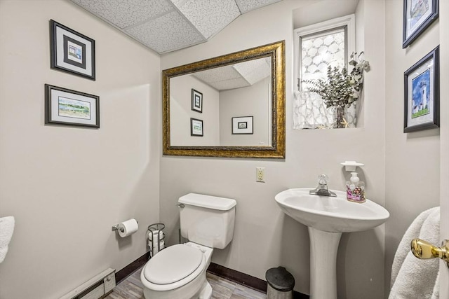 half bathroom with toilet, baseboards, baseboard heating, and a drop ceiling