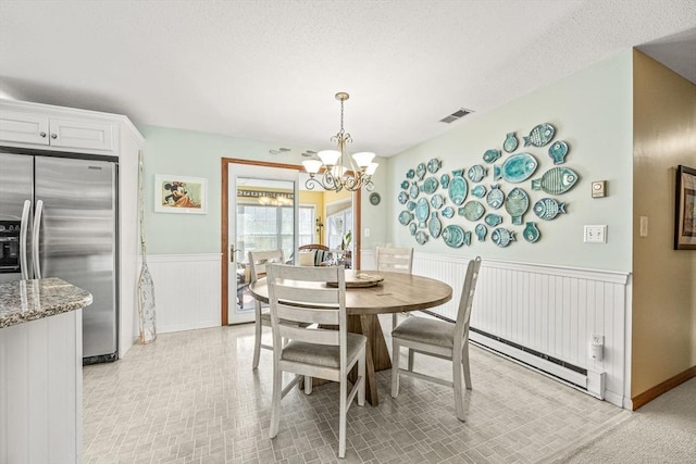 dining space featuring a wainscoted wall, visible vents, baseboard heating, an inviting chandelier, and a textured ceiling