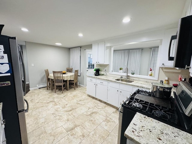 kitchen with freestanding refrigerator, a sink, range with gas cooktop, a baseboard radiator, and tasteful backsplash
