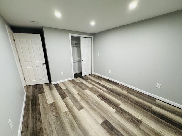unfurnished bedroom featuring baseboards, wood finished floors, a closet, and recessed lighting