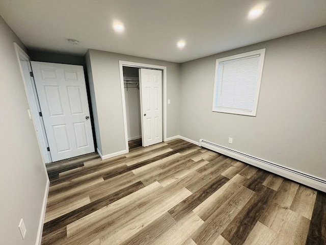 unfurnished bedroom with a baseboard radiator, wood finished floors, baseboards, recessed lighting, and a closet