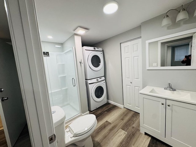 bathroom featuring stacked washing machine and dryer, a stall shower, toilet, wood finished floors, and vanity