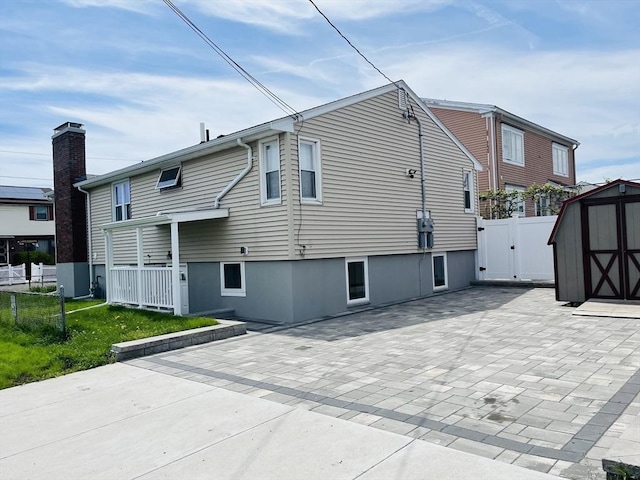 rear view of property with a shed, a patio, an outdoor structure, fence, and a gate