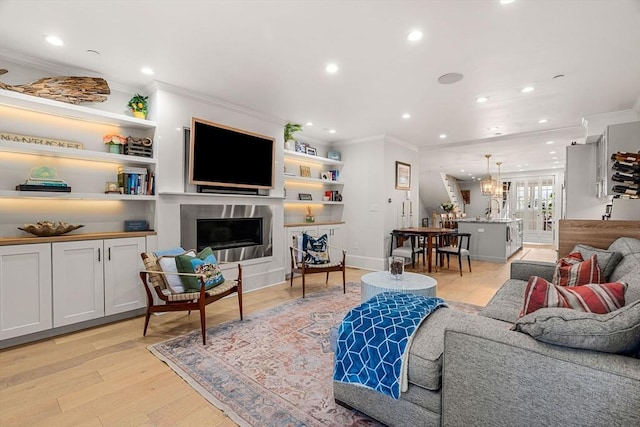 living room with crown molding, built in features, light hardwood / wood-style flooring, and sink