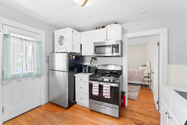 92 Winthrop Shore Dr Unit 2, Winthrop, MA 02152 - kitchen featuring stainless steel appliances, stacked washer and clothes dryer, white cabinetry, light wood-type flooring, and light countertops