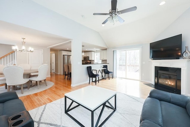 living room with baseboards, a fireplace with flush hearth, vaulted ceiling, light wood-type flooring, and ceiling fan with notable chandelier