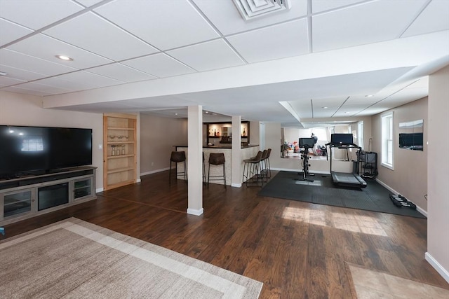 workout room featuring built in shelves, dark wood finished floors, visible vents, a drop ceiling, and baseboards