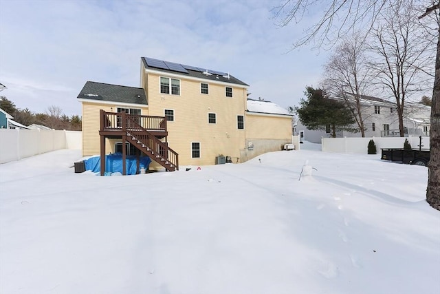 snow covered back of property featuring roof mounted solar panels, fence, stairway, and a wooden deck