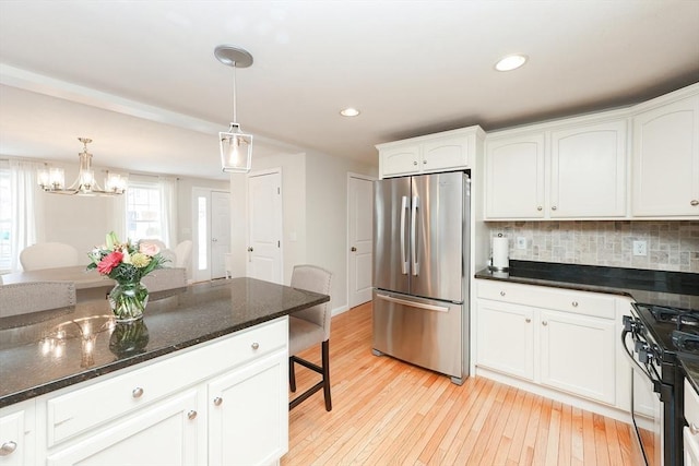 kitchen with white cabinets, range, freestanding refrigerator, dark stone countertops, and pendant lighting