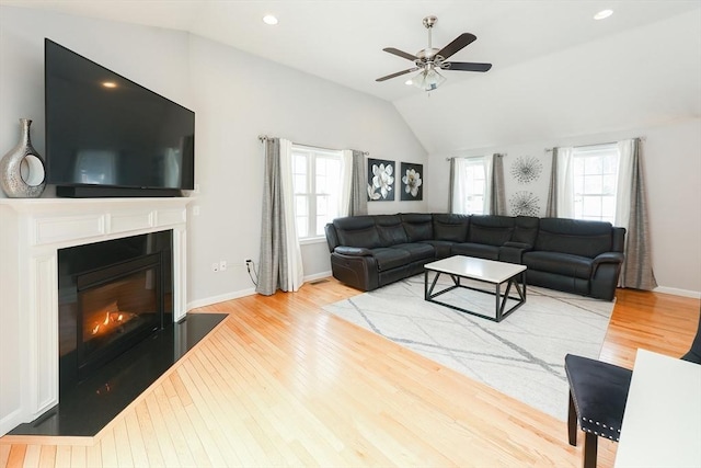 living area with vaulted ceiling, wood finished floors, a glass covered fireplace, and a healthy amount of sunlight