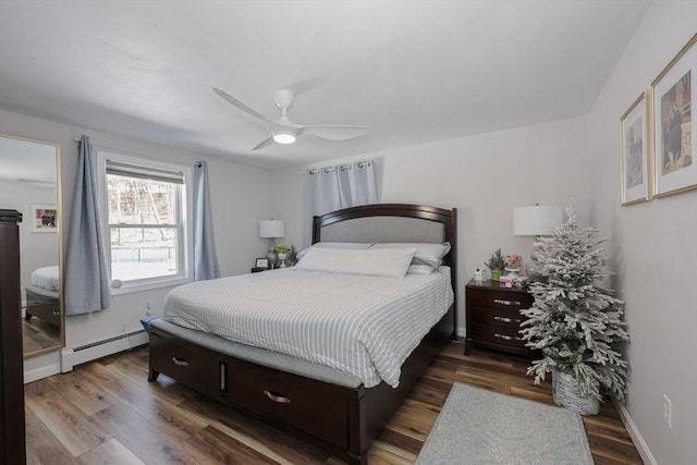 bedroom with a baseboard heating unit, wood finished floors, and baseboards