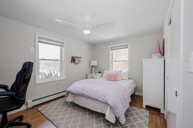 bedroom with ceiling fan, multiple windows, baseboard heating, and wood finished floors