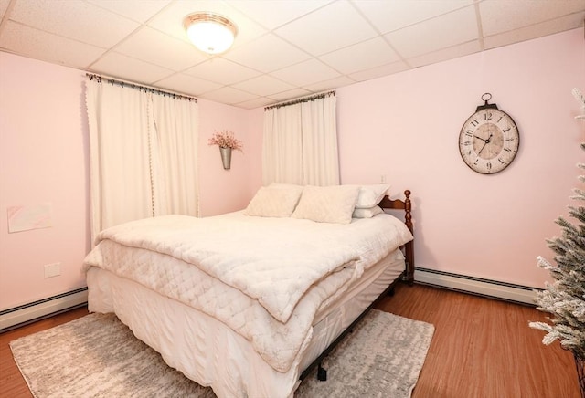 bedroom featuring a paneled ceiling, a baseboard radiator, and wood finished floors