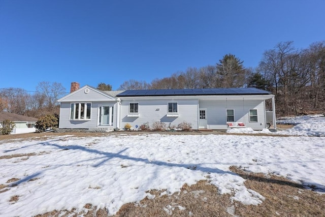 snow covered rear of property with entry steps, roof mounted solar panels, and a chimney