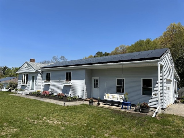 rear view of house featuring a garage, roof mounted solar panels, a chimney, and a yard