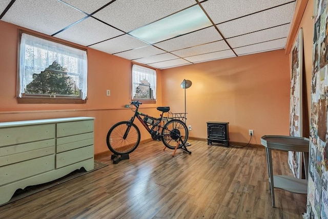 workout area with a wood stove, wood finished floors, baseboards, and a drop ceiling