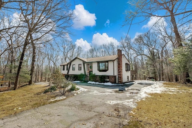 raised ranch featuring aphalt driveway, a chimney, and brick siding