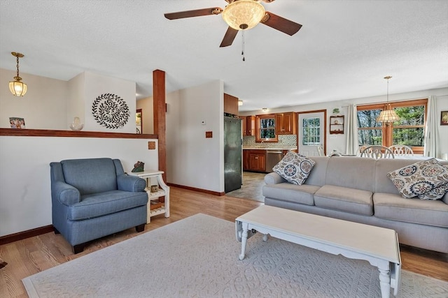 living room featuring a textured ceiling, baseboards, light wood-style floors, and a ceiling fan