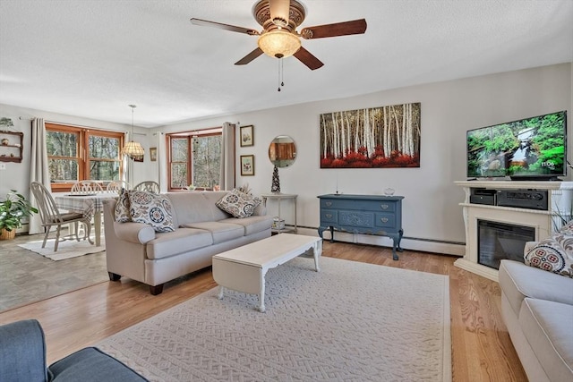 living room featuring a glass covered fireplace, light wood-style flooring, ceiling fan with notable chandelier, and a baseboard radiator