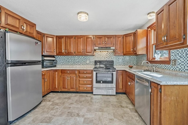 kitchen with under cabinet range hood, appliances with stainless steel finishes, brown cabinetry, and a sink