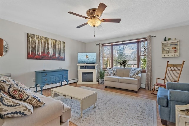 living area featuring a glass covered fireplace, wood finished floors, ceiling fan, a textured ceiling, and a baseboard heating unit