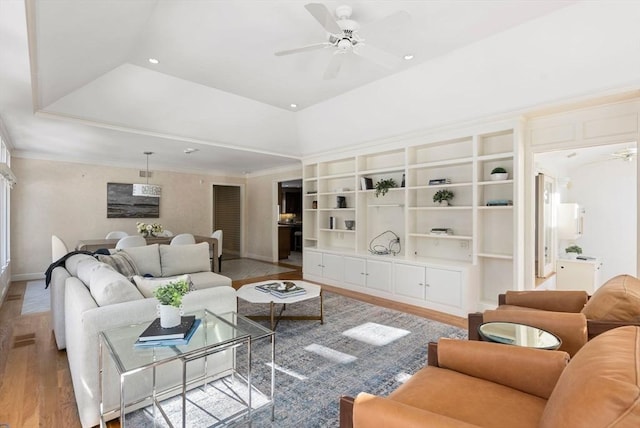 living room featuring a tray ceiling, ornamental molding, ceiling fan, and light wood-type flooring